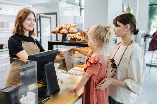 Friendly cashier handing pastry goods in a bag to mom with a daughter. stock photo