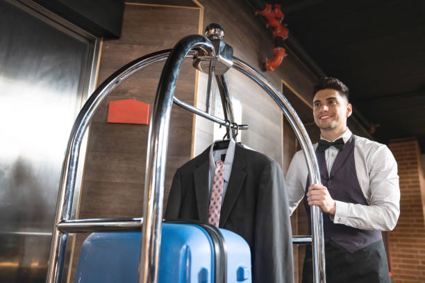 Friendly concierge at hotel pushing luggage cart with a bag and suit of customer at a luxury hotel Friendly concierge at hotel pushing luggage cart with a bag and suit of customer at a luxury hotel - Low angle view luggage cart stock pictures, royalty-free photos & images