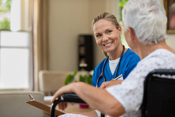 Friendly nurse talking to senior patient Friendly doctor examining health of patient sitting in wheelchair. Happy smiling nurse consulting disabled patient about treatment. Nurse caring about elder handicap man at home. female nurse stock pictures, royalty-free photos & images