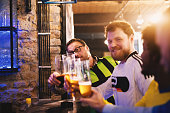 Friendly soccer fans are sitting at the pub counter and saluting each other while wishing each other a good luck in upcoming game.