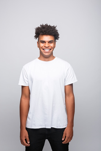 Portrait of cheerful young man wearing white t-shirt. Male student smiling at camera. Studio shot, grey background.