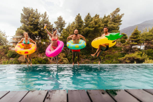 Friends are jumping into the pool Friends with inflatable rings jumping in the swimming pool vacation rental photos stock pictures, royalty-free photos & images