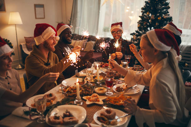 Friends Celebrating Christmas Together Multi-ethnic group of people holding sparklers while enjoying Christmas dinner at home dinner stock pictures, royalty-free photos & images