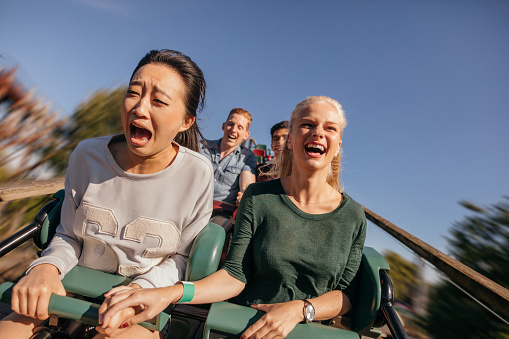 Shot of young friends cheering and riding roller coaster at amusement park. Young people having fun on rollercoaster.
