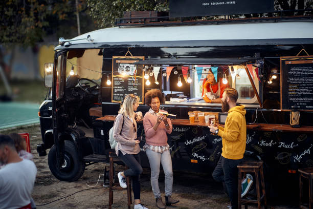 friends eating, drinking, talking, socializing outdoor in front of modifed truck for fast food service group of friends eating, drinking, talking, socializing outdoor in front of modifed truck for fast food service food truck stock pictures, royalty-free photos & images