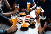 Male friends with beer glasses and snacks sitting at table in pub. Men enjoying drinks during weekend in restaurant. They are spending leisure time together.