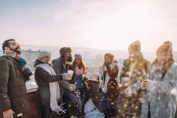 Friends enjoying sunny winter day outdoors Smiling group of friends drinking hot drinks outdoors, on the sunny winter afternoon. They are at the rooftop terrace that overlooks the city. snow party stock pictures, royalty-free photos & images