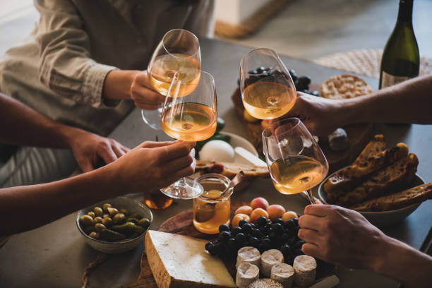 Friends having wine tasting or celebrating event with wine Glasses of white orange or rose wine in hands of celebrating friends over table with various gourmet snacks cheese grape bread. Gathering, celebrating, wine tasting and party concept wine photos stock pictures, royalty-free photos & images
