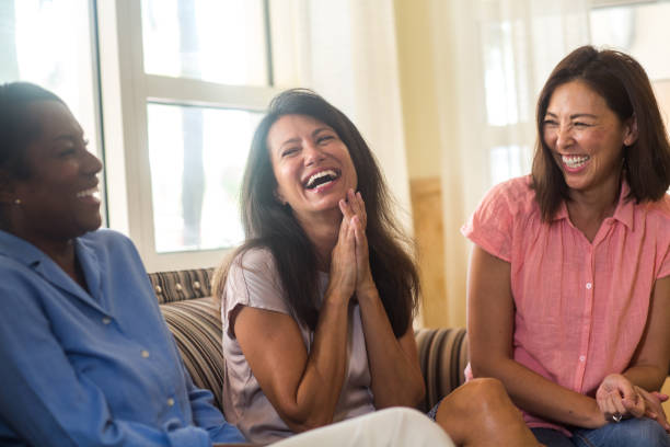 Friends laughing and talking sitting at home on the sofa stock photo