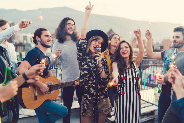 Friends on the rooftop listening to a guitar singer Group of friends enjoying a guitar party with solo performance on the rooftop individual event stock pictures, royalty-free photos & images