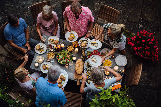 Friends Outdoors Dining A group of mature friends are sitting around an outdoor dining table, eating and drinking. They are all talking happily and enjoying each others company. The image has been shot from above and taken in Tuscany, Italy. dinner party stock pictures, royalty-free photos & images