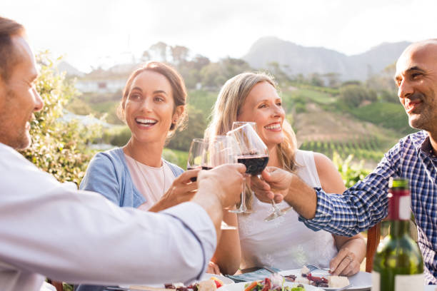 Friends raising toast Happy friends raising their glasses in a toast outdoor in a winery farm. Smiling mature woman and men enjoying a picnic together at park. Middle aged multiethnic couple having dinner together and toasting wine."r mid adult couple stock pictures, royalty-free photos & images