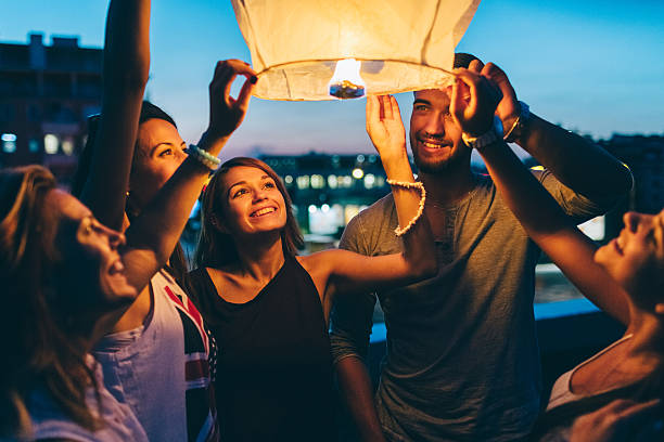 Friends releasing paper lantern for New Year Happy friends on a rooftop party holding a sky lantern new years eve girl stock pictures, royalty-free photos & images