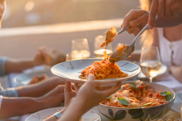 Friends Serving spaghetti Bolognese on a table at sunset. There are glasses of wine and salad on the table; close up tight crop stock photo