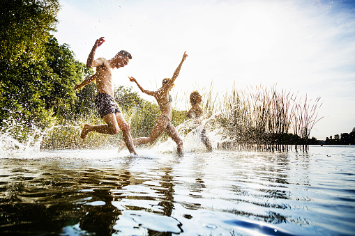 A group of friends excitedly splashing in the water on a day out at the lake together.