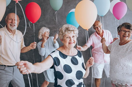 Smiling grandmother wearing blouse with black dots during New Year's Eve party with friends holding colorful balloons