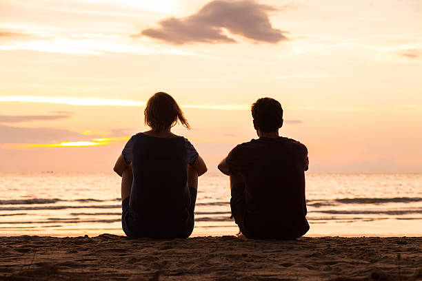 友情、ビーチで一緒に座っている友人 - 夕日の海辺 ストックフォトと画像