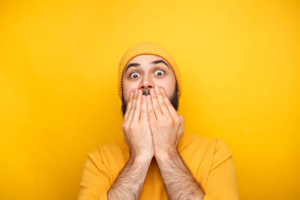 Frightened man in yellow clothes Scared and frightened young man in yellow clothes with hands up to mouth. worried man funny stock pictures, royalty-free photos & images