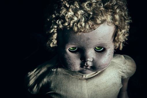 A dirty vintage baby doll in the dark with green evil eyes.