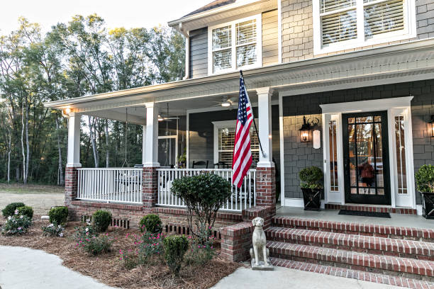 Front door entrance to a large two story blue gray house with wood and vinyl siding and a large American flag. stock photo