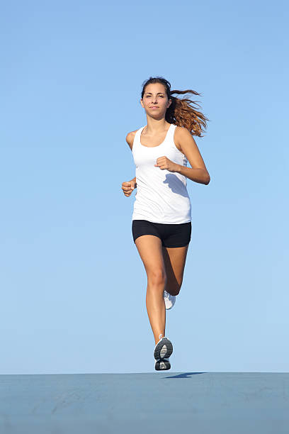 Front view of a beautiful sportswoman running towards camera Front view of a beautiful sportswoman running towards camera with the blue sky in the background approaching stock pictures, royalty-free photos & images