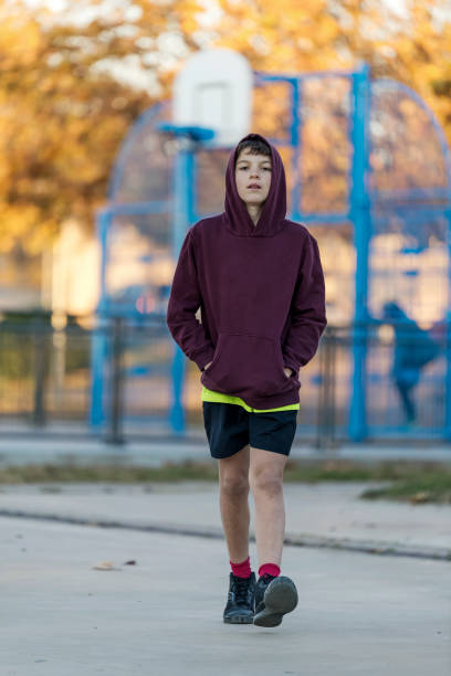 Front view of a young hooded boy walking away stock photo