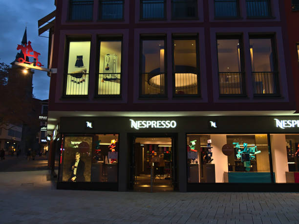 vue avant du magasin de détail nespresso (capsules de café) avec des vitrines illuminées sur la place du marché au centre-ville dans la soirée. - nespresso photos et images de collection