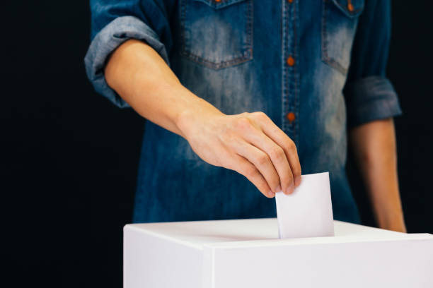 Front view of person holding ballot paper casting vote at a polling station for election vote in black background Front view of person holding ballot paper casting vote at a polling station for election vote in black background voting booth stock pictures, royalty-free photos & images