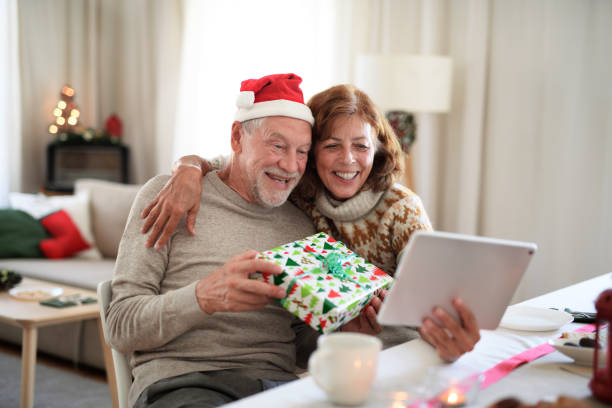 front view of senior couple indoors at home at christmas, having video call with family. - woman holding a christmas gift imagens e fotografias de stock