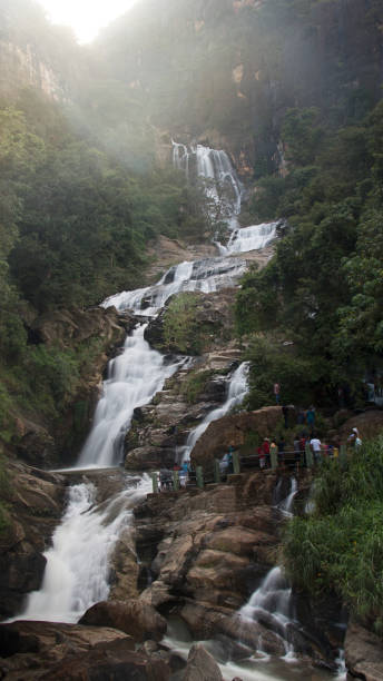 Front view vertical Long-exposure of cascading rocky Ravana Falls in Ella, Sri Lanka with visitors and sun rays above the waterfall stock photo