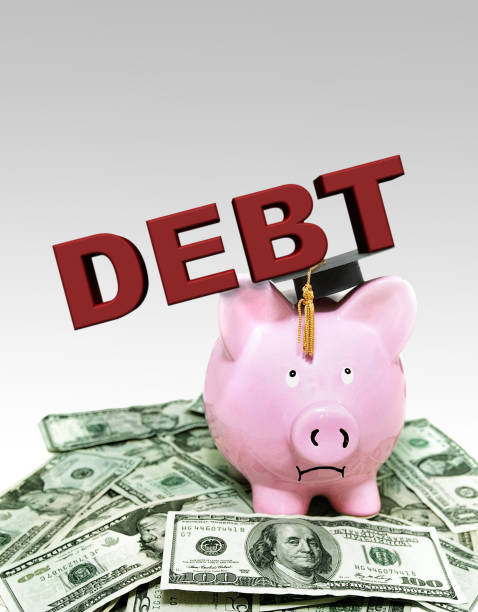 Frowning piggy bank under Debt text with graduation cap, on a pile of money Frowning piggy bank under Debt text with graduation cap, on a pile of money student loan forgiveness foreigh stock pictures, royalty-free photos & images