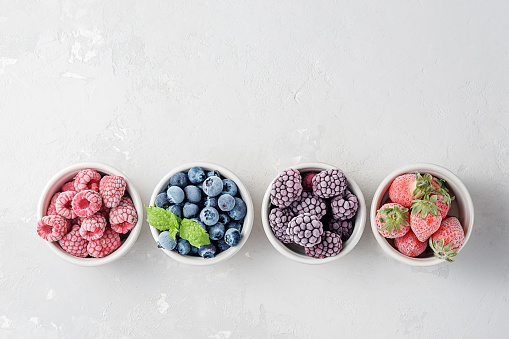 Frozen berries in small bowls on a concrete background from copies of space.