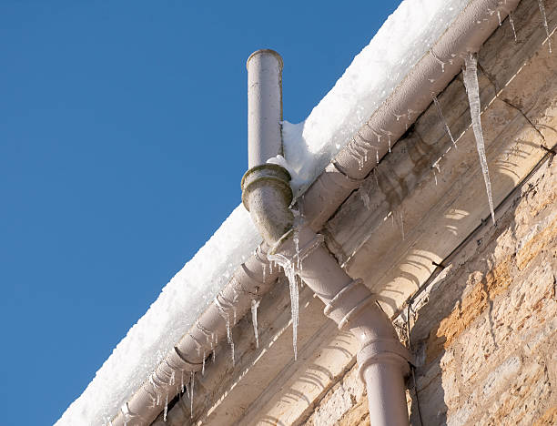 Frozen Gutter Icicles hanging from the gutter, and snow on the roof causing drainage problems for an old building in winter. frozen water stock pictures, royalty-free photos & images