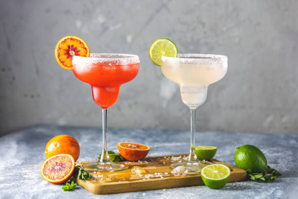 Frozen lime margarita and blood orange margarita cocktail mix in salt rimmed glasses garnished with slices of lime and orange. Focus on the citrus slice stock photo