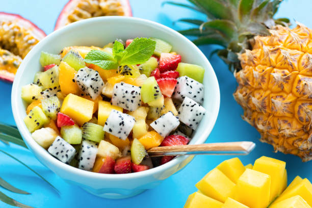 Fruit salad in bowl on blue background Fruit salad in bowl on blue background. Exotic tropical fruit salad. Dragon fruit, passion fruit, mango, coconut, strawberry and pineapple salad in a bowl fruit salad stock pictures, royalty-free photos & images