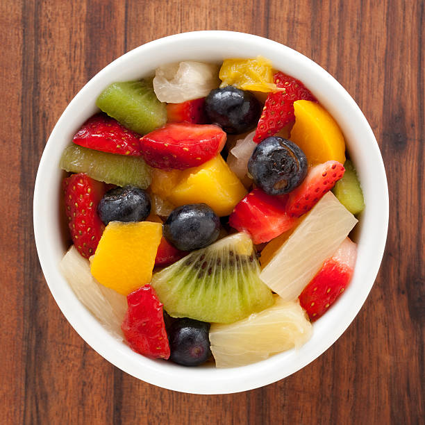 Fruit salad Top view of white bowl full of fruit salad containing strawberries, blueberries, orange, kiwi, pineapple and peach fruit salad stock pictures, royalty-free photos & images