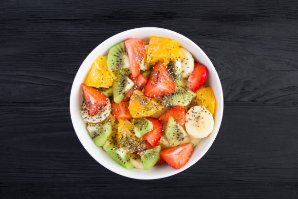 Fruit salad with chia seed in the white  bowl in the center of  the black wooden background. Top view. Close-up. stock photo