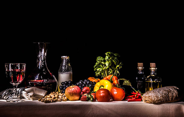 Fruit, vegetables, milk, wine, oil, vinegar, bread A light painting photograph showing fruit, vegetables, milk, wine, oil, vinegar, bread on a set table against a dark dramatic background giving it the look and feel of a renaissance flemish painting still life stock pictures, royalty-free photos & images