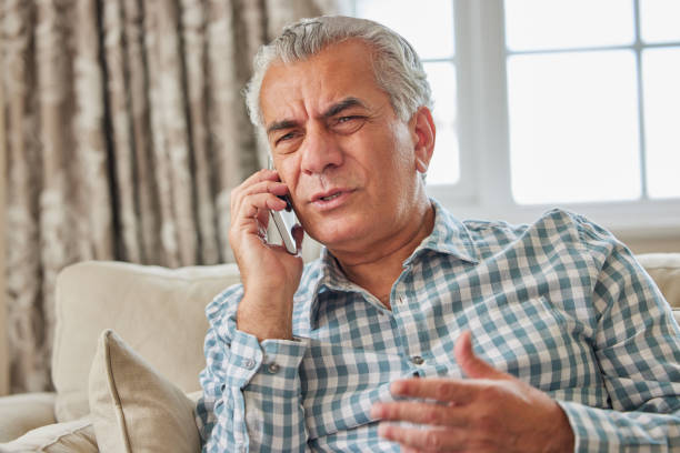 Frustrated Mature Man Receiving Unwanted Telephone Call At Home stock photo
