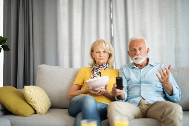 Frustrated senior husband and wife watching television together. stock photo