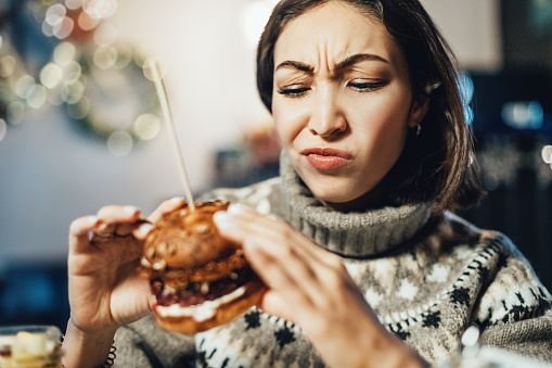 A frustrated woman frowns because she can't feel the aroma and taste of a hamburger, which is an important and first symptom of the covid-19 coronavirus