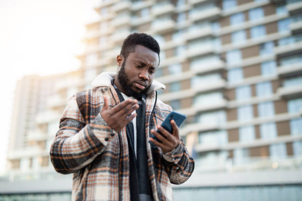 Frustrated young man using phone. Unhappy African American man looking at phone. frustration stock pictures, royalty-free photos & images