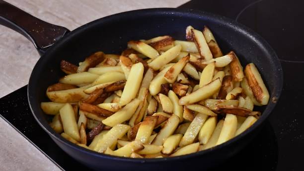 Frying homemade French fries in pan on kitchen stove stock photo