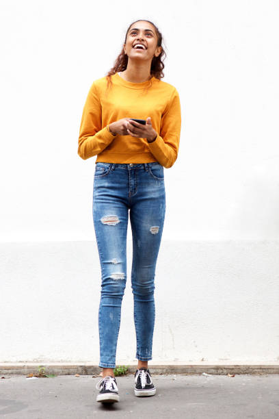 Full body beautiful young woman smiling by white wall with cellphone Full body portrait of beautiful young woman smiling by white wall with cellphone indian women walking stock pictures, royalty-free photos & images