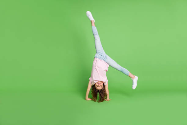 Full body photo of young little girl stand on hand acrobat sporty training isolated over green color background stock photo