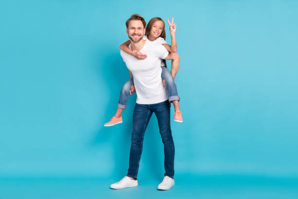 Full body portrait of cheerful guy hold on back piggyback carefree pupil show v-sign isolated on blue color background stock photo