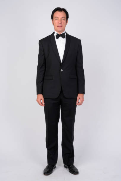 Full body shot of mature handsome businessman standing against white background Studio shot of mature handsome businessman wearing tuxedo against white background tuxedo stock pictures, royalty-free photos & images