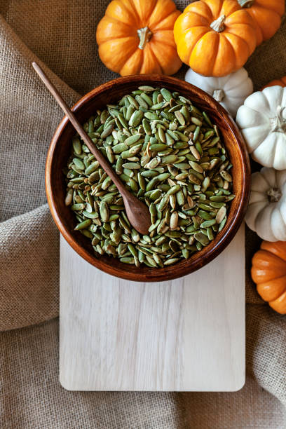 Full bowl of pumpkin seeds closeup on a cutting board with colorful pumpking around stock photo