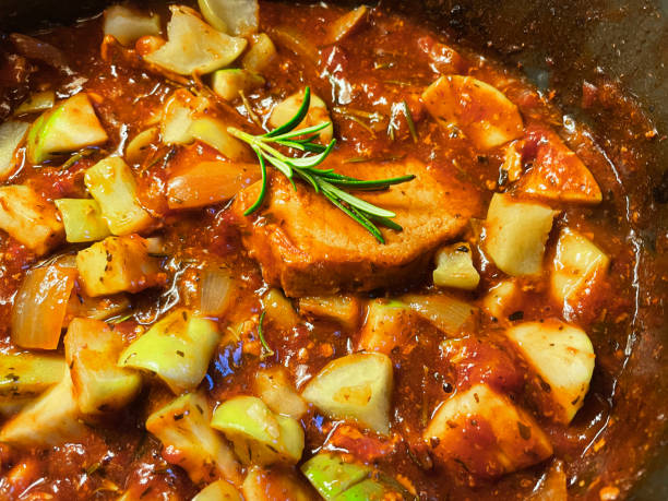 Full frame image of homemade pork and apple casserole in cider sauce gravy with diced Granny Smith apple being cooked in slow cooker with fresh Rosemary herb sprigs, flavoursome tomato gravy sweet and savoury pork stew elevated view, focus on foreground stock photo