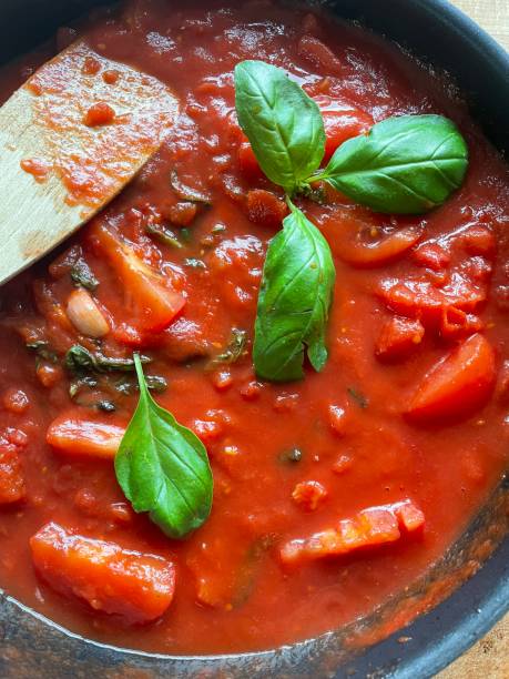 Full frame image of tomato sauce cooking in frying pan being stirred by a wooden spatula, green basil leaves, elevated view stock photo